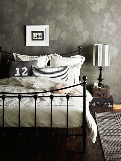 Dormitorio en blanco y negro con cama de hierro, maletas vintage y papel pintado